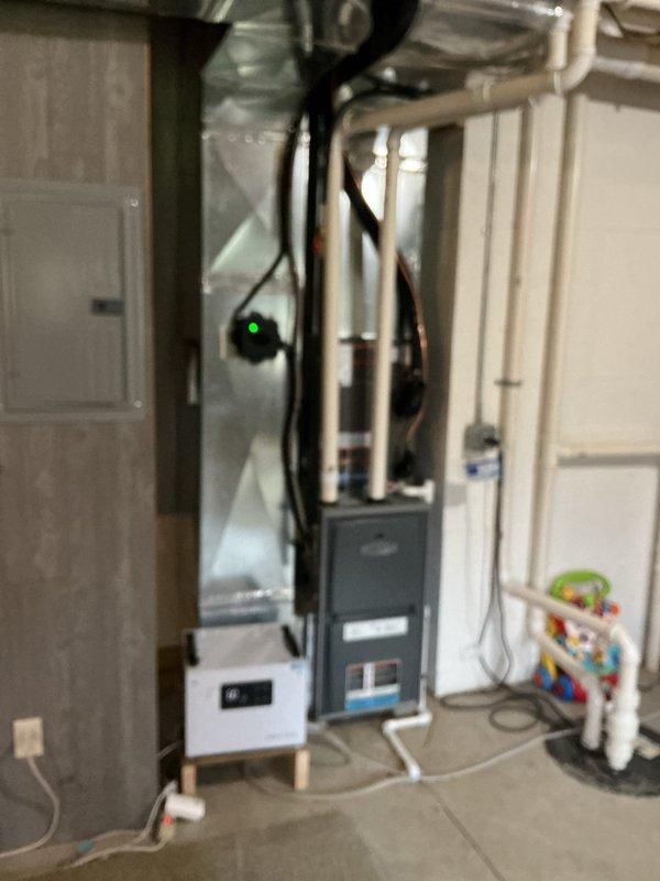 Completed new construction HVAC installation including Lennox condenser unit mounted on exterior platform with proper PVC condensate drainage routing along building exterior. Interior basement installation features furnace with connected ductwork and air handler, all mechanical systems commissioned and operational with power confirmed via LED indicators.