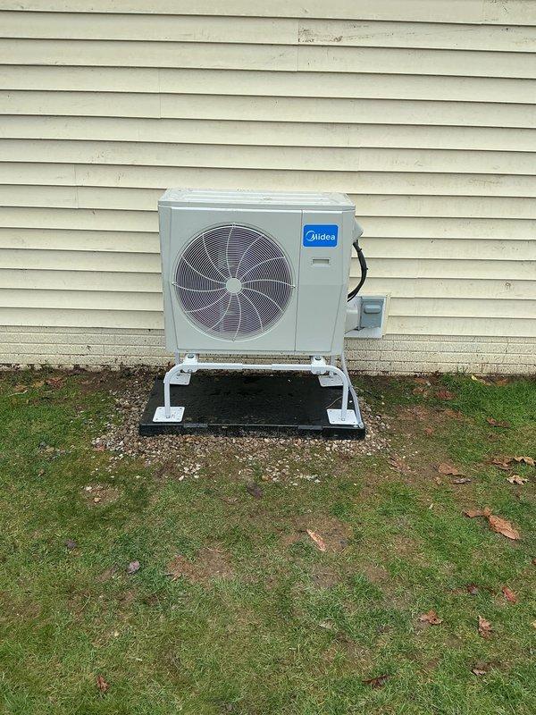 Completed new construction HVAC installation featuring dual Midea outdoor units mounted on white composite pads with proper gravel base for drainage and stability. Installed refrigerant line sets with weather-resistant insulation, established electrical connections with exterior disconnect box, and penetrated building envelope with appropriate sealing to maintain energy efficiency. All equipment positioned per manufacturer specifications with adequate clearances for service access and airflow, system tested and operational.