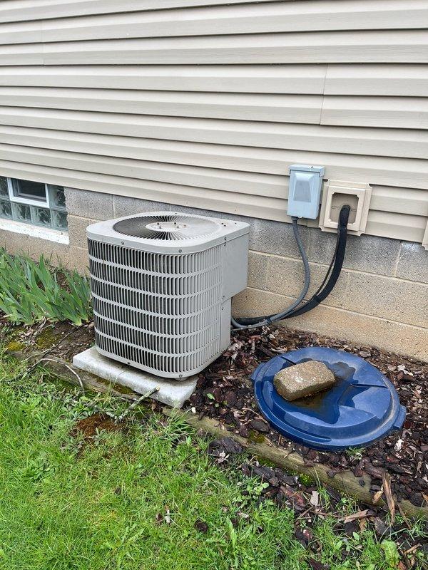 Completed AC retrofit installation at residential property. Installed new furnace unit in basement utility area with associated ductwork modifications, including vertical metallic supply plenum and horizontal distribution connections. Replaced outdoor condensing unit on existing concrete pad with new gray cylindrical condenser, verified proper electrical connections to wall-mounted disconnect and power supply, and confirmed system operational functionality upon startup.
