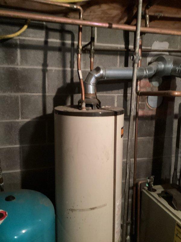 Conducted comprehensive assessment of existing water heater installation in basement utility area. Evaluated 40-50 gallon capacity water heater with copper supply and distribution piping connected at top of unit. Documented severe corrosion and rust deterioration on base pan and floor area beneath water heater, indicating previous or ongoing leak conditions. Inspected mechanical components, pressure tank, and associated plumbing connections for proper operation and code compliance. Photographed current installation configuration including copper piping runs, PVC drainage, wall-mounted supports, and corroded base assembly to provide detailed documentation for water heater replacement estimate.