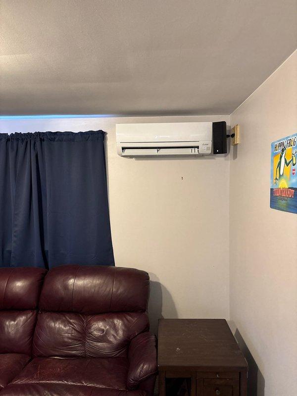 Completed installation of ductless mini-split system in basement with indoor unit mounted on interior wall and outdoor condenser positioned under deck. Line set was concealed along exterior of building using protective channel, with refrigerant lines and control wiring routed from basement unit to outdoor condenser. Connected system to existing electrical supply and performed startup, vacuum, and refrigerant charge procedures to ensure proper operation.