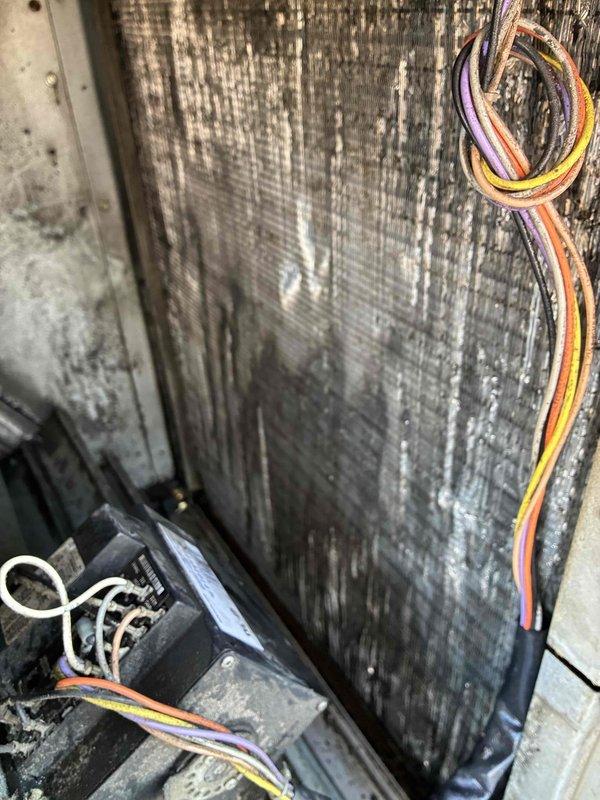 Completed scheduled commercial cooling maintenance visit on HVAC system. Inspected evaporator coil assembly and found significant dust and debris accumulation on heat exchanger fins with visible yellow-tan staining indicating possible contamination or moisture-related residue buildup. Documented electrical wiring connections and metallic housing components showing vertical streaking patterns consistent with normal operational wear and environmental exposure. System requires coil cleaning to restore optimal heat transfer efficiency and prevent potential performance degradation.