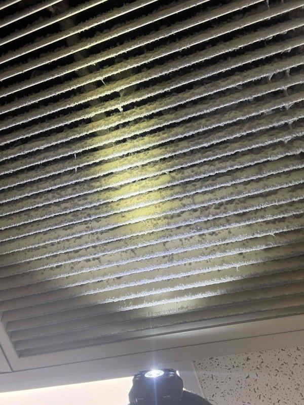 Completed scheduled commercial cooling maintenance visit on HVAC system. Inspected evaporator coil assembly and found significant dust and debris accumulation on heat exchanger fins with visible yellow-tan staining indicating possible contamination or moisture-related residue buildup. Documented electrical wiring connections and metallic housing components showing vertical streaking patterns consistent with normal operational wear and environmental exposure. System requires coil cleaning to restore optimal heat transfer efficiency and prevent potential performance degradation.