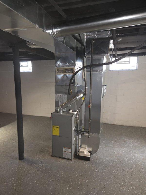 Completed new construction HVAC ductwork installation in basement mechanical room, including full trunk line and branch duct system fabricated from galvanized metal with proper hangers and support strapping secured to ceiling joists. Installed and positioned gray furnace/air handler unit on concrete floor with all necessary connections, ensuring proper clearances and access for future maintenance per manufacturer specifications.