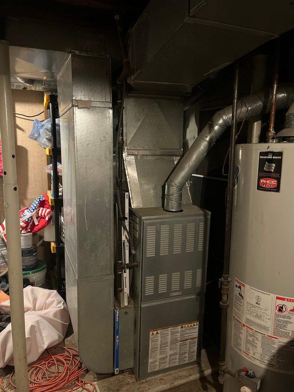 Completed site assessment for AC add-on installation in residential basement utility area. Documented existing HVAC infrastructure including furnace unit, ductwork configuration, and water heater placement to determine optimal integration points for new air conditioning system and evaluate spatial requirements for equipment installation.