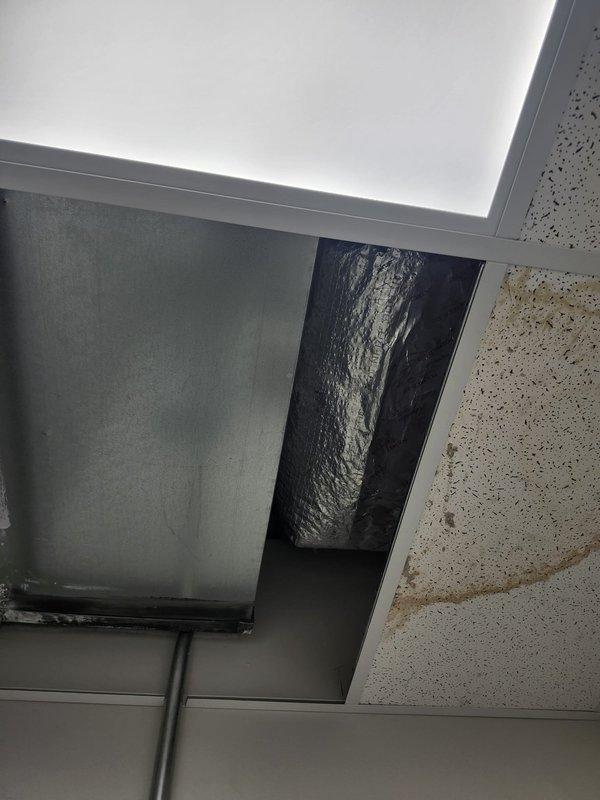 Responded to commercial A/C leak complaint and conducted thorough inspection of rooftop unit and interior ceiling plenum. Located source of water intrusion at rooftop drain assembly with deteriorated connections and inadequate sealing, causing water to migrate through ceiling penetrations where flexible ductwork enters conditioned space. Documented standing water with algae growth around drain fitting, compromised insulation materials, and evidence of chronic moisture exposure on rooftop surface. Identified flexible duct penetration in ceiling grid system as secondary leak point where condensate and rainwater infiltration were entering building interior. Recommended immediate repair of rooftop drainage system, replacement of deteriorated drain fittings and surrounding weatherproofing, cleaning of affected rooftop surfaces to remove biological growth, and proper sealing of all ceiling penetrations around ductwork to prevent future water intrusion.