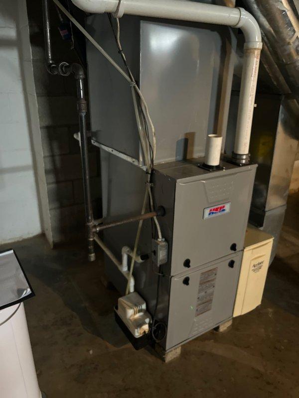 Completed air conditioning retrofit evaluation and comprehensive furnace condition assessment at residential property. Inspected existing HVAC system including beige cabinet-style furnace unit mounted on concrete blocks, verified proper installation of metallic ductwork connections, and examined PVC venting system, electrical conduit, and associated components. Documented current equipment specifications, ductwork configuration, and overall system condition through detailed photography for replacement estimate preparation.