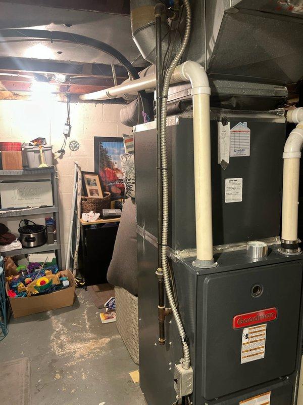 Completed full HVAC system retrofit including outdoor condenser unit installation in side yard location and indoor Goodman furnace installation in basement utility area. Outdoor unit positioned between building structures with proper clearances maintained despite narrow access corridor and overgrown vegetation. Indoor furnace installed with PVC venting system, condensate drainage lines, and flexible ductwork connections integrated with existing distribution system. All equipment commissioned and tested for proper operation.