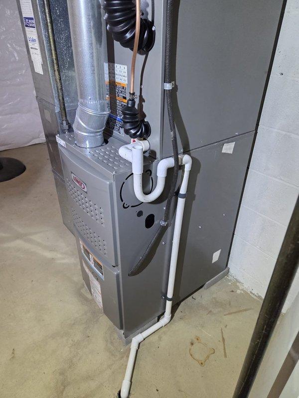 Completed residential air conditioning retrofit installation in basement utility area. Installed new Lennox furnace system with coordinating evaporator coil, integrated with existing ductwork infrastructure. System includes proper condensate drainage using white PVC piping with secure mounting, galvanized sheet metal supply ductwork with vibration isolation components, and black flexible return ducting. All equipment properly positioned against concrete block walls with adequate clearances for service access and code compliance. Installation verified operational with all connections secured and labeled per manufacturer specifications.