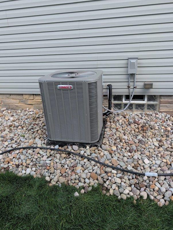 Completed full AC retrofit installation featuring a new Lennox outdoor condensing unit with matching evaporator coil system. Unit was positioned on concrete pad with river rock landscaping, electrical disconnect and line set connections properly installed and secured to building exterior per manufacturer specifications. All refrigerant lines, condensate drainage, and electrical wiring terminated according to code requirements, system tested and verified operational.