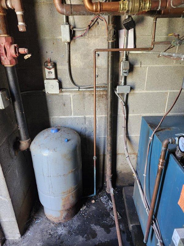 Responded to emergency water leak from pressure relief valve on boiler system. Upon arrival, found boiler and associated valves had been shut off by occupant to stop active discharge. Inspected pressure tank, piping connections, and relief valve assembly in basement mechanical room. Documented existing conditions including aged pressure tank with visible rust staining, moisture accumulation on floor around tank base, and complete copper piping configuration connecting to wall-mounted components. Photographed system layout showing pressure tank, pump assembly, electrical components, and piping network for diagnostic and record purposes.
