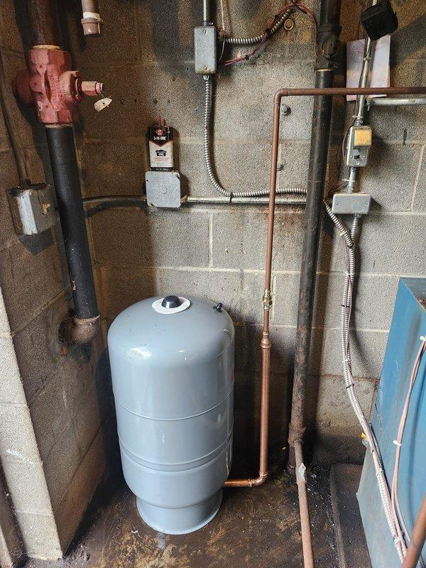 Responded to emergency water leak from pressure relief valve on boiler system. Upon arrival, found boiler and associated valves had been shut off by occupant to stop active discharge. Inspected pressure tank, piping connections, and relief valve assembly in basement mechanical room. Documented existing conditions including aged pressure tank with visible rust staining, moisture accumulation on floor around tank base, and complete copper piping configuration connecting to wall-mounted components. Photographed system layout showing pressure tank, pump assembly, electrical components, and piping network for diagnostic and record purposes.