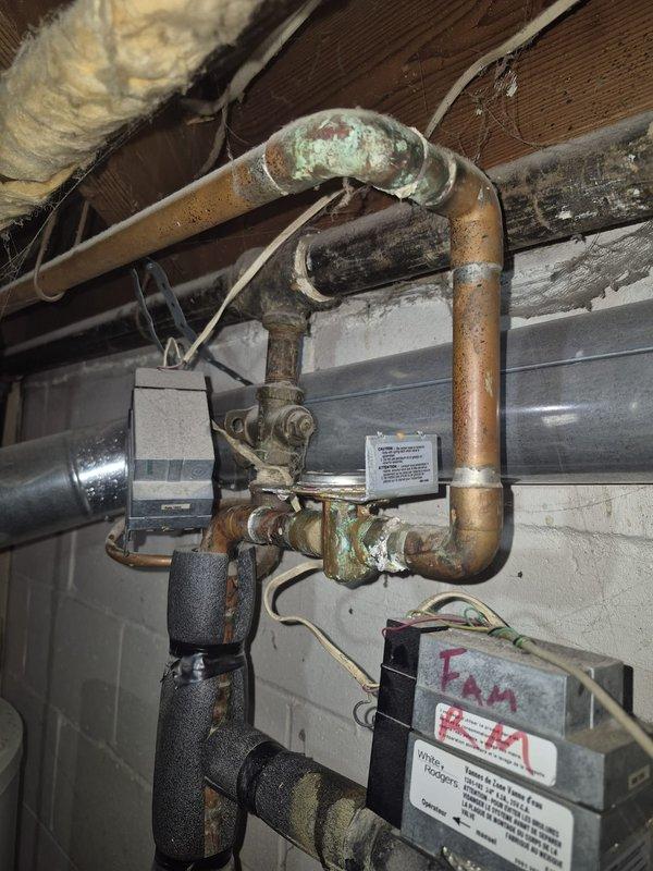 Responded to service call for reported boiler leak in basement mechanical area. Upon inspection, discovered significant corrosion and oxidation on copper piping assembly, particularly on bypass loop configuration with visible green patina at multiple joints and connection points. Assessed electrical relay component connected to circulator pump system, noting age-related wear on terminals and wiring connections. Documented extensive deterioration of mechanical system components including corroded piping and aging control devices. Photographed affected areas showing compromised copper pipe integrity and electrical connections for repair recommendations. System requires replacement of corroded copper piping sections and evaluation of pump relay functionality to restore proper operation and eliminate active leak source.