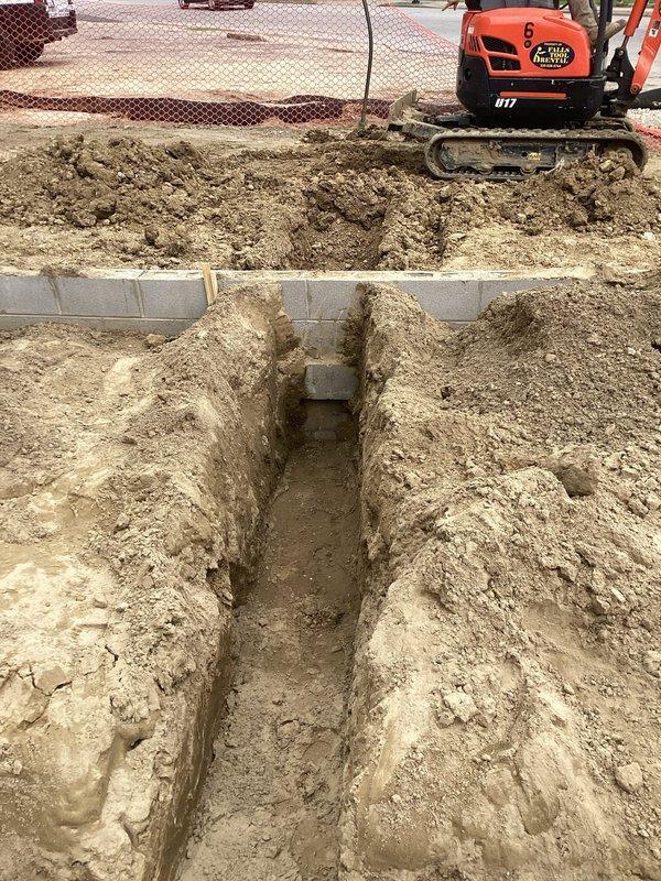 Completed rough-in plumbing installation for bathroom facilities at new construction site. Excavated trench using mini excavator in sandy soil conditions, installed white PVC drainage piping system including main lines, branch connections, and various fittings such as elbows and Y-connectors to accommodate multiple fixture locations. All pipes positioned and staged for final connection and testing prior to backfill.