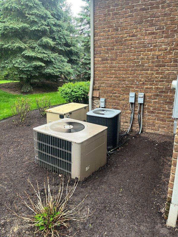 Completed full HVAC system replacement including installation of dual furnace units, central air handler, and two outdoor condensing units. Interior basement installation features organized PVC venting, copper refrigerant line sets, and integrated ductwork connections for multi-zone climate control. Exterior condensers positioned on prepared gravel pad with proper electrical disconnects, conduit routing, and refrigerant line connections secured to building exterior.