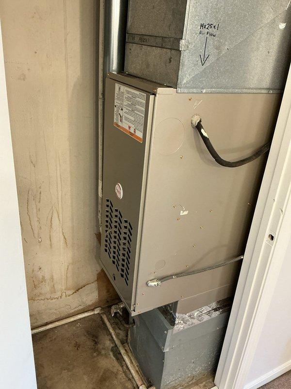 Completed water heater replacement in residential utility closet with removal and reinstallation of existing HVAC furnace to accommodate new tanked water heater unit. Disconnected and properly removed old water heater, temporarily relocated furnace equipment to provide adequate workspace and clearance for new installation. Installed new gray metallic cylindrical water heater with appropriate connections including copper supply piping at top and black flexible supply lines at base. Reinstalled beige HVAC air handler unit in proper position adjacent to water heater, ensuring adequate clearance and ventilation requirements per manufacturer specifications and local code. Verified all ductwork connections including rectangular metal plenum and flexible black ducting remained secure and properly sealed. Confirmed water heater venting, temperature and pressure relief valve, and all plumbing connections meet code requirements. System tested and operational upon completion.