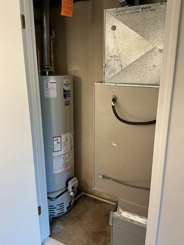 Completed water heater replacement in residential utility closet with removal and reinstallation of existing HVAC furnace to accommodate new tanked water heater unit. Disconnected and properly removed old water heater, temporarily relocated furnace equipment to provide adequate workspace and clearance for new installation. Installed new gray metallic cylindrical water heater with appropriate connections including copper supply piping at top and black flexible supply lines at base. Reinstalled beige HVAC air handler unit in proper position adjacent to water heater, ensuring adequate clearance and ventilation requirements per manufacturer specifications and local code. Verified all ductwork connections including rectangular metal plenum and flexible black ducting remained secure and properly sealed. Confirmed water heater venting, temperature and pressure relief valve, and all plumbing connections meet code requirements. System tested and operational upon completion.
