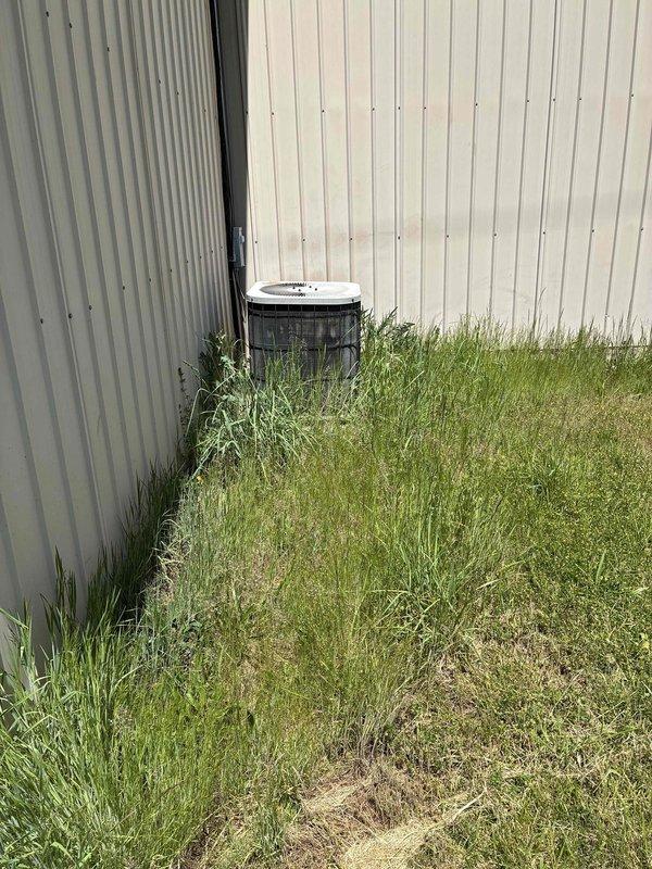 Completed routine commercial cooling maintenance visit on outdoor HVAC condenser unit. Performed standard inspection and documented system condition with thermostat showing normal operation range. Noted vegetation overgrowth around exterior unit requiring clearance maintenance to ensure proper airflow and system efficiency.
