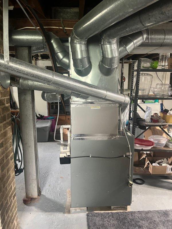 Completed full HVAC system retrofit in basement utility area, replacing existing furnace and air conditioning equipment. New furnace unit installed on concrete pad with proper clearances from brick wall, connected to existing ductwork infrastructure including multiple supply branches extending to upper levels. All metallic ductwork connections secured and sealed, with galvanized metal ducts properly fitted to new equipment specifications. System tested for proper airflow distribution and operational functionality upon completion.