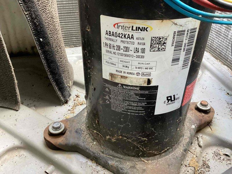 Responded to service call for non-operational commercial A/C unit located in back mechanical space. Upon inspection, found InterLINK compressor model ABA042KAA (R410A refrigerant) showing signs of age with visible corrosion on mounting pan and base components. Evaluated air handler unit, condensate drain lines, and refrigerant line set; confirmed proper drainage and verified system connections. Documented equipment condition including compressor specifications and overall installation for service records.
