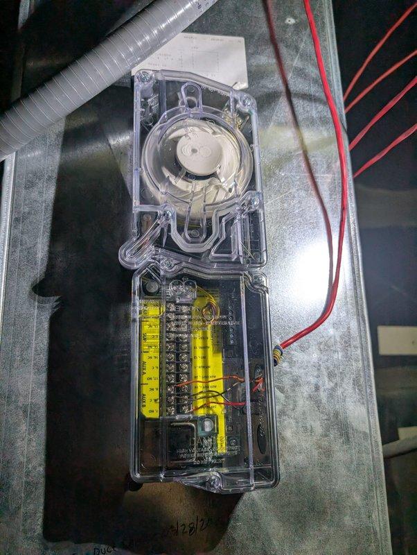 Installed new duct smoke detector on commercial HVAC air handler unit. Device was mounted to the top cabinet surface with clear protective housing containing internal electrical components, motor assembly, and proper wiring connections. Unit tested and operational upon completion.
