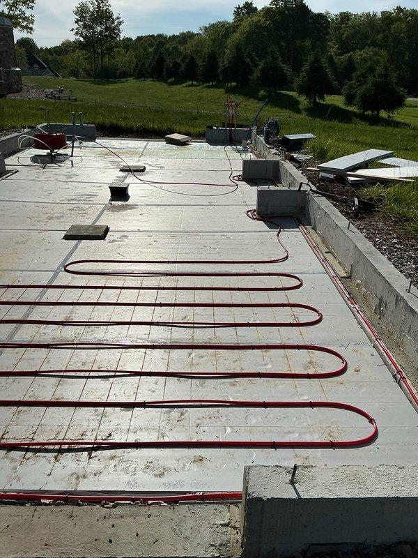# HVAC New Construction Install

Completed installation of radiant heating system on new construction concrete foundation slab. Installed multiple parallel runs of red PEX tubing in serpentine loop configuration across entire slab surface. Tubing secured and positioned systematically with proper spacing for optimal heat distribution. Junction boxes placed at strategic intervals along tubing runs for system connectivity and control. Installation performed on prepared concrete foundation with anchor bolts in place, ready for next phase of construction. System layout designed for efficient radiant floor heating operation in new residential structure.