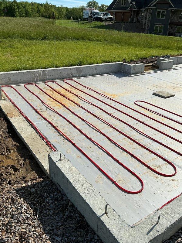 # HVAC New Construction Install

Completed installation of radiant heating system on new construction concrete foundation slab. Installed multiple parallel runs of red PEX tubing in serpentine loop configuration across entire slab surface. Tubing secured and positioned systematically with proper spacing for optimal heat distribution. Junction boxes placed at strategic intervals along tubing runs for system connectivity and control. Installation performed on prepared concrete foundation with anchor bolts in place, ready for next phase of construction. System layout designed for efficient radiant floor heating operation in new residential structure.