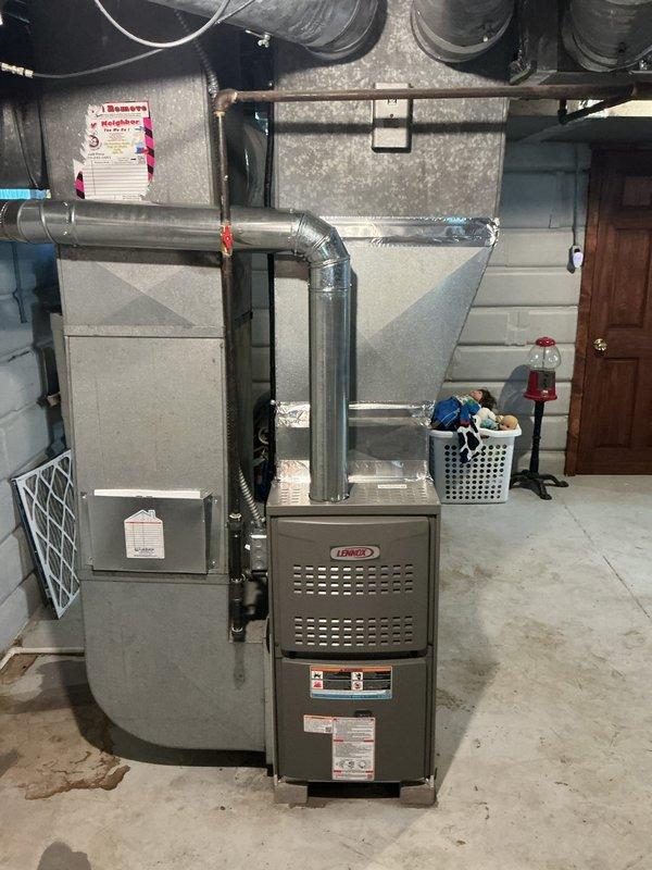 Completed furnace retrofit installation in residential basement utility room, removing existing aged air handler unit and installing new gray Lennox furnace system. Connected all necessary ductwork including gray metal supply plenum and flexible return ducting, installed white PVC condensate drain line, and verified proper electrical connections and system operation upon completion.