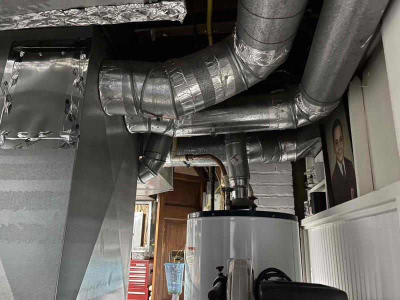 Performed preventive maintenance on 20+ year old air conditioning system. Inspected outdoor condensing unit located in below-grade corrugated metal enclosure, removed accumulated leaves and organic debris from concrete pad and unit perimeter, and checked refrigerant line insulation condition. Evaluated indoor ductwork system with reflective insulation wrapping and verified proper mechanical connections throughout the installation.