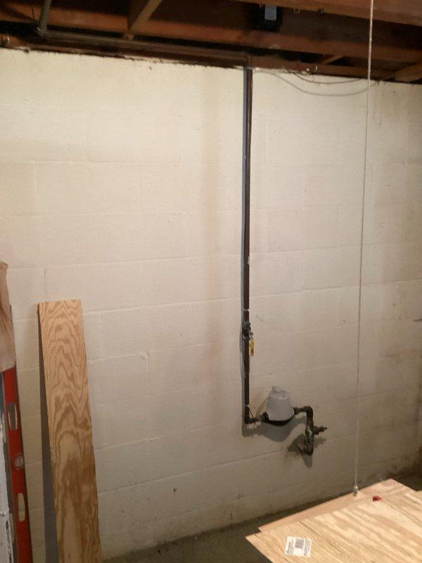 Replumbed backyard spigot connection to main water supply line in basement crawl space. Installed new black supply pipe with shutoff valve and hose connection, securing all components to cinder block foundation wall per code requirements.
