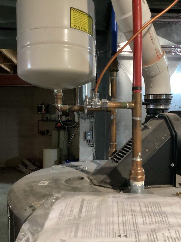 Responded to reported hot water tank leak at residential property. Upon inspection, identified active leak condition on 75-gallon capacity water heater unit manufactured in Mexico with AHRI certification. Assessed expansion tank, copper piping connections, and associated brass fittings for integrity and proper operation. Documented equipment specifications, including thermal efficiency rating of 80% and standby loss of 1045 BTU/HR. Verified installation compliance with ASHRAE/IESNA standards and confirmed all safety warning labels were properly displayed regarding flammable vapor hazards. Photographed equipment configuration showing expansion tank mounting, copper supply lines with visible solder joints, circulation pump assembly, and related plumbing connections for service records.