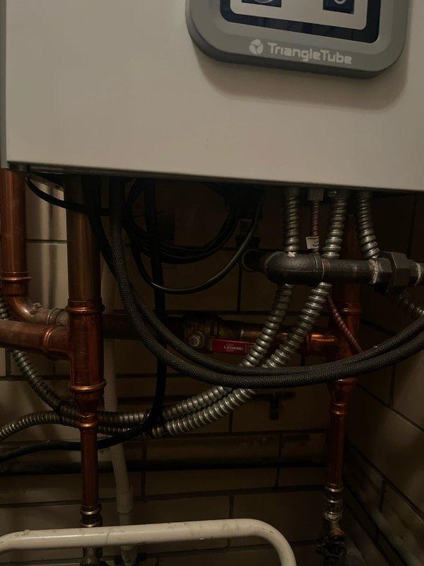 Completed boiler retrofit involving the replacement of an existing Triangle Tube boiler unit. Installation included reconnection of copper supply lines, flexible metallic hoses, and integration with existing PVC drainage system, ensuring all plumbing connections were properly secured and tested for system functionality.