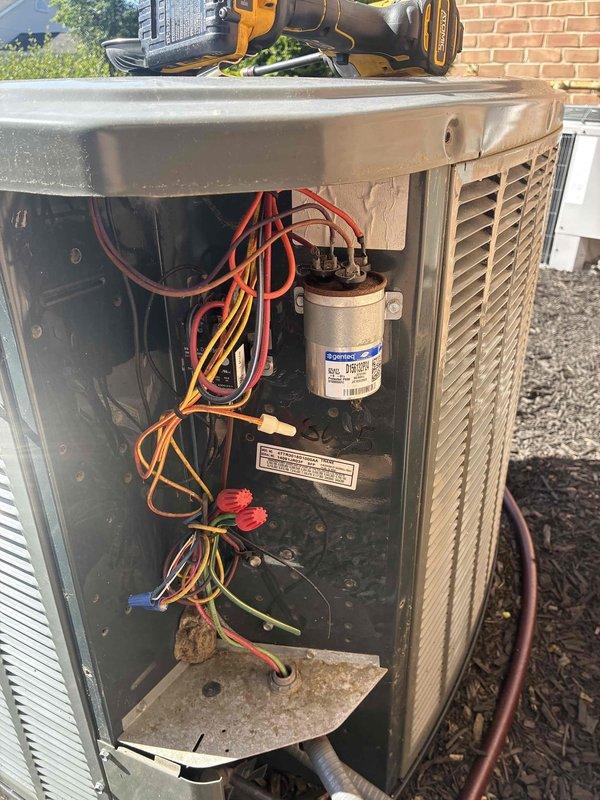 Completed comprehensive spring maintenance on Trane outdoor air conditioning condenser unit. Performed detailed inspection of all accessible components including capacitor, electrical connections, wiring harnesses, and refrigerant lines. Verified proper operation of condenser fan assembly and protective guard, checked electrical connections with red wire nuts for security, and inspected the condition of the cylindrical capacitor with all terminal connections. Examined exterior cabinet for weathering and structural integrity, confirmed refrigerant lines and electrical conduit properly secured along building exterior, and verified unit placement on pad with adequate clearance from brick wall. All components found to be in functional operating condition with normal seasonal wear patterns observed on exterior surfaces.