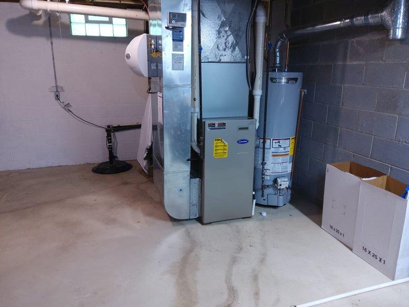 Completed full HVAC system retrofit in residential basement utility room, replacing existing furnace and air conditioning equipment with new Carrier-branded units. Installed new furnace, air handler, and associated ductwork connections to ceiling-mounted distribution system. All equipment positioned and secured on concrete floor with proper clearances maintained from existing water heater and utility systems. System tested and verified operational upon completion.