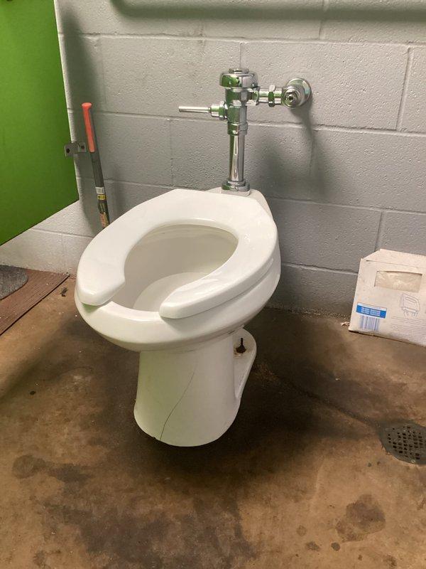 Responded to service call for non-flushing toilet in service bathroom with reported cracking. Upon inspection, found wall-mounted flush valve toilet system with damaged porcelain fixture requiring replacement. Removed existing cracked toilet bowl and wall-mounted chrome flush valve assembly. Installed new white porcelain toilet fixture with updated flush valve hardware and supply line connections. Tested flush mechanism for proper operation and verified all connections for leaks. System restored to full working order with new hardware installed.