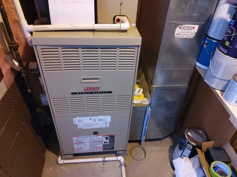 Completed full HVAC system retrofit installation in residential basement utility area. Installed new Lennox Merit Series gas furnace with associated white PVC venting and condensate drainage piping, along with metallic ductwork and air handler components. Connected copper refrigerant lines with shut-off valves, routed black flexible conduit for electrical connections, and integrated system with existing infrastructure between exposed wall studs with fiberglass insulation.