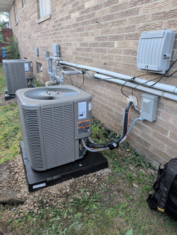 # HVAC Install - Complete System

## Summary
Completed full HVAC system retrofit including new furnace and air conditioning condenser installation with associated refrigerant lines, electrical connections, and PVC drainage system.

## Work Performed

Removed existing HVAC equipment and installed new complete heating and cooling system. Positioned air conditioning condenser unit on protective pad over gravel base against exterior brick wall. Ran and insulated refrigerant line set from outdoor condenser to indoor evaporator coil. Installed gray PVC condensate drainage piping system with proper pitch and routing along exterior wall.

Mounted electrical disconnect boxes and junction boxes on exterior brick wall per code requirements. Ran electrical conduit and wiring to power outdoor condenser unit. Connected refrigerant lines with proper flare fittings and insulation wrapping.

In basement utility area, installed new furnace unit with reflective foil-wrapped supply plenum and ductwork con