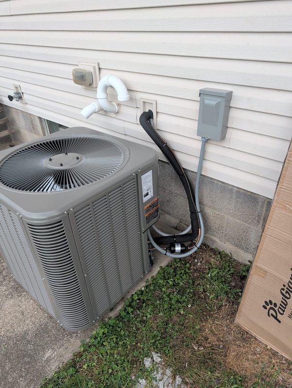 # HVAC Install - A/C & Coil

Completed full AC retrofit installation including outdoor condensing unit and indoor evaporator coil system. Installed new gray air conditioning condenser on concrete pad with proper clearances from structure. Mounted coil assembly to existing furnace system in basement utility area. Ran refrigerant lines between outdoor and indoor components with proper insulation and securing methods. Installed black electrical conduit from condensing unit to wall-mounted disconnect box with appropriate wire sizing for unit specifications. Configured white PVC condensate drain line from evaporator coil with proper pitch and termination point exterior to building. Connected system to existing ductwork and verified all connections sealed properly. Tested electrical connections at both indoor and outdoor units. Performed refrigerant charge verification and system startup procedures. Confirmed proper airflow across evaporator coil and through duct system. Verified condensing 