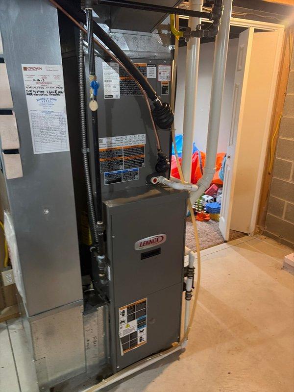 # AC Retrofit Installation

Completed a comprehensive AC retrofit installation in residential basement utility room. Installed new Lennox furnace system with integrated evaporator coil unit and connected all necessary ductwork to existing HVAC infrastructure. Ran black flexible conduit and refrigerant lines from outdoor condensing unit to indoor air handler, ensuring proper insulation and secure mounting. Installed electrical disconnect panel with appropriate labeling and wiring diagrams for code compliance. Connected white PVC condensate drain lines with proper pitch and trap configuration, routing to floor drain with auxiliary condensate pump for backup protection. Mounted all equipment on existing tile floor with proper clearances for service access and airflow. Verified all electrical connections, tested system startup and operation, confirmed proper refrigerant charge and airflow through supply ductwork. System operational and performing to manufacturer specifications.