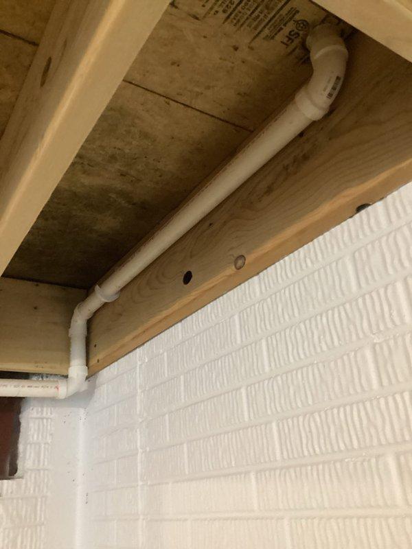Responded to a fully backed-up kitchen drain with no drainage in a nine-year-old residence. Accessed the plumbing system through the rear of the property and inspected the drain line configuration, including the white PVC drainage piping running through the ceiling joists and structural framing. Successfully cleared the blockage in the kitchen sink drain line, restoring full drainage functionality to the black double-basin sink. Tested water flow through the faucet to verify proper drainage and confirm the system was operating correctly with no standing water or slow drainage issues remaining.