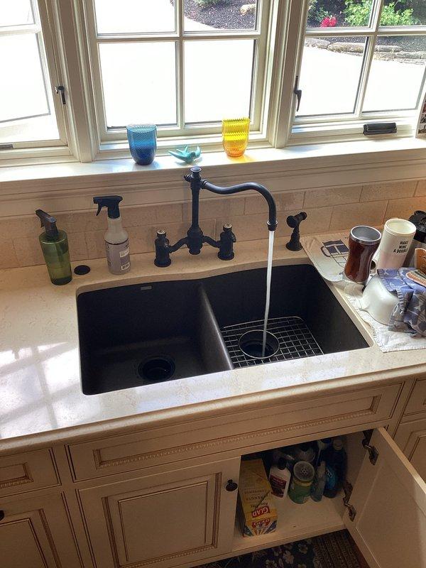 Responded to a fully backed-up kitchen drain with no drainage in a nine-year-old residence. Accessed the plumbing system through the rear of the property and inspected the drain line configuration, including the white PVC drainage piping running through the ceiling joists and structural framing. Successfully cleared the blockage in the kitchen sink drain line, restoring full drainage functionality to the black double-basin sink. Tested water flow through the faucet to verify proper drainage and confirm the system was operating correctly with no standing water or slow drainage issues remaining.