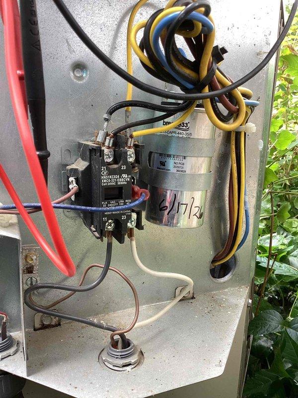 Completed scheduled commercial cooling maintenance visit on outdoor condensing unit. Inspected electrical components including contactor, capacitor (marked 4/7/21), and associated wiring connections within control panel. Observed operational equipment with signs of normal wear and environmental exposure. Unit accessible but surrounded by vegetation growth requiring clearance consideration for proper airflow. All electrical connections visually inspected and equipment photographed for maintenance records.