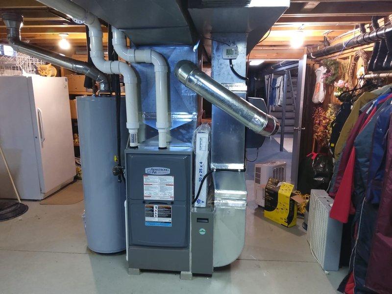 Completed AC retrofit installation in residential basement utility area. Installed new gray metal furnace unit with associated white PVC venting pipes and metallic supply ductwork, positioned centrally for optimal airflow distribution. System integration included proper connection to existing ductwork infrastructure and venting configuration routed through upper ceiling joists to exterior termination point.