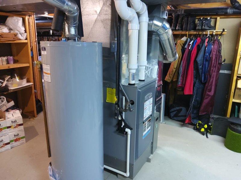 Completed AC retrofit installation in residential basement utility area. Installed new gray metal furnace unit with associated white PVC venting pipes and metallic supply ductwork, positioned centrally for optimal airflow distribution. System integration included proper connection to existing ductwork infrastructure and venting configuration routed through upper ceiling joists to exterior termination point.