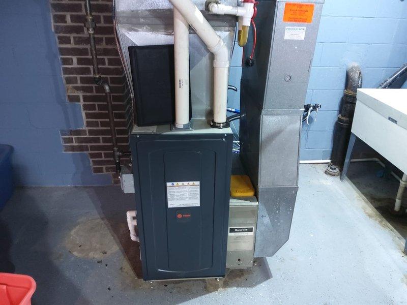 Completed AC retrofit installation in basement mechanical room. Installed new dark gray furnace unit with white PVC venting system for proper exhaust and intake air management. Positioned equipment on concrete floor alongside existing HVAC components including air handler unit. Configured all necessary piping connections, electrical conduit, and safety labeling per manufacturer specifications and code requirements. System tested and verified operational.