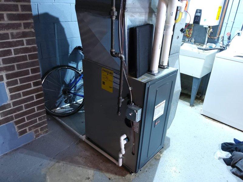 Completed AC retrofit installation in basement mechanical room. Installed new dark gray furnace unit with white PVC venting system for proper exhaust and intake air management. Positioned equipment on concrete floor alongside existing HVAC components including air handler unit. Configured all necessary piping connections, electrical conduit, and safety labeling per manufacturer specifications and code requirements. System tested and verified operational.