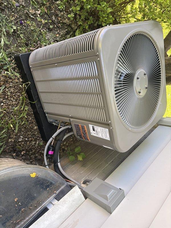 # HVAC Install - A/C & Coil

Completed full AC retrofit installation at residential property. Removed existing air conditioning system and installed new outdoor condenser unit on concrete pad with proper elevation and clearance from structure. Unit positioned on white base platform with appropriate spacing for airflow and serviceability.

Installed new evaporator coil inside existing air handler. Ran new refrigerant line set from outdoor condenser to indoor coil, utilizing gray insulation material on copper piping for proper temperature control and condensation prevention. Secured refrigerant lines with mounting clips along building exterior, routing lines efficiently to minimize exposure and maintain clean appearance.

Installed electrical disconnect box on exterior wall adjacent to condenser unit, mounted on vinyl siding per code requirements. Completed all electrical connections between disconnect, condenser unit, and indoor air handler. Verified proper voltage and amperage at equip