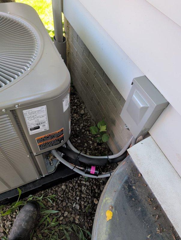 # HVAC Install - A/C & Coil

Completed full AC retrofit installation at residential property. Removed existing air conditioning system and installed new outdoor condenser unit on concrete pad with proper elevation and clearance from structure. Unit positioned on white base platform with appropriate spacing for airflow and serviceability.

Installed new evaporator coil inside existing air handler. Ran new refrigerant line set from outdoor condenser to indoor coil, utilizing gray insulation material on copper piping for proper temperature control and condensation prevention. Secured refrigerant lines with mounting clips along building exterior, routing lines efficiently to minimize exposure and maintain clean appearance.

Installed electrical disconnect box on exterior wall adjacent to condenser unit, mounted on vinyl siding per code requirements. Completed all electrical connections between disconnect, condenser unit, and indoor air handler. Verified proper voltage and amperage at equip