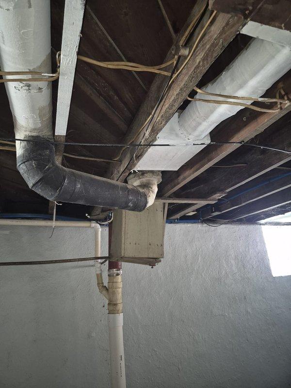 # HVAC Service Call - No Airflow from Two Registers

Responded to service call regarding lack of airflow from two registers in the home. Upon arrival, conducted visual inspection of the HVAC distribution system in the basement/crawlspace area to identify the source of the airflow issue.

Performed thorough examination of the ductwork routing and connections serving the affected registers. Inspected the main trunk lines and branch ducts for potential obstructions, disconnections, or damage that could restrict airflow. Evaluated the condition of flexible ductwork runs, noting dust accumulation and age-related wear on black flexible ducting visible in the ceiling cavity.

Assessed the structural support and mounting of ductwork components, checking metal strapping and brackets securing ducts to floor joists. Verified that insulated supply lines were properly installed and not compressed or kinked, which could impede air distribution to specific zones.

Traced ductwork pathways through the