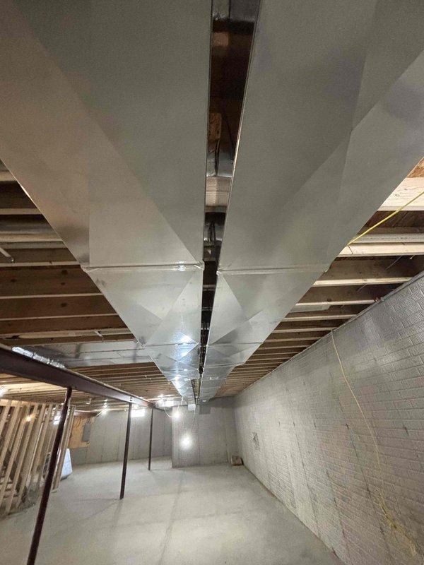 Completed new construction HVAC ductwork installation in unfinished basement mechanical space. Installed and secured multiple runs of rectangular sheet metal supply and return ductwork throughout the space using metal strapping and hangers attached to floor joists and structural supports. All ductwork properly sized, sealed, and suspended to building code specifications to serve the conditioned spaces above.